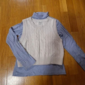 Vitbeige kabelstickad väst från Lindex med ljusblå polotröja - Superfin beige stickad väst från Lindex Kids i storlek 134/140. Västen har klassiskt kabelstickat mönster, ribbade kanter vid hals, ärmhål och nederkant. Perfekt att slänga över en skjorta eller långärmad tröja. Med på köpet får du en mjuk långärmad polo. Blålila