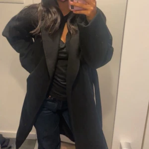 Svart kappa med bälte - Säljer en svart lång kappa med bälte i midjan och stora fickor. Jackan har en rak och oversized passform med långa ärmar och enkel design🩷