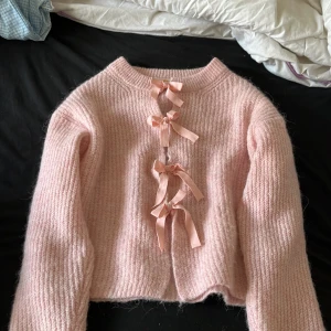 Rosa kofta med rosetter från Gina Tricot - Superfin ljusrosa stickad kofta från Gina Tricot med tre söta rosetter framtill. Koftan är croppad och har långärmad modell, perfekt för att ge en gullig touch till din outfit.