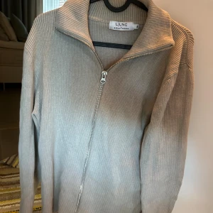 Beige ribbad kofta från Ljung - Säljer en stilren beige ribbad kofta från Ljung by Marcus Larsson i storlek S. Koftan har lång ärm, hög krage och hel dragkedja framtill. Perfekt för lager-på-lager och passar till jeans eller chinos.