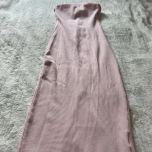 Ljusrosa axelbandslös långklänning - Säljer en ljusrosa axelbandslös långklänning med smal ribbad struktur och slits baktill. Klänningen har en figurnära passform och är perfekt för dig som gillar en stilren och feminin look.