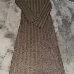 Brun ribbad långärmad klänning - Mysig brun långärmad klänning i ribbat material. Klänningen har en rak passform och är i en längre modell, perfekt för dig som gillar en enkel men stilren look. Passar till sneakers eller boots för en chill vibe.