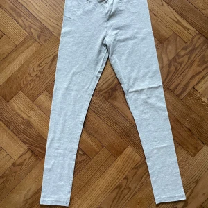 Ljusgrå leggings från Åhléns - Snygga ljusgrå leggings från Åhléns i mjukt och stretchigt material. Tillverkade av 90% ekologisk bomull, 5% elastan och 5% viskos. De har en smal passform och är perfekta för chill dagar eller när du vill ha något bekvämt.