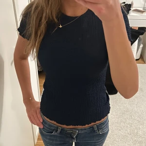 Mörkblå tröja  - Säljer en mörkblå smockad topp med korta ärmar och rund halsringning. Toppen har en tight passform och vågig kant nertill för en snygg detalj. 