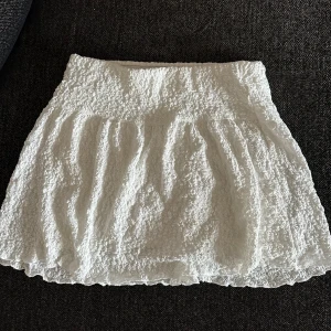 Vit kortkjol från Gina Tricot - Supersöt vit kortkjol från Gina Tricot med krispig struktur och lätt volang i nederkant. 🤍oanvänd