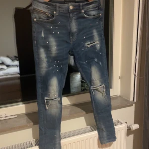 Supply & Demand blå jeans  - Blå skinny jeans från Supply & Demand med slitna detaljer, hål på knäna och färgstänk framtill. Jeansen har dragkedja vid fickan, klassisk femficksdesign och är tillverkade i stretchigt denim för en tight passform.