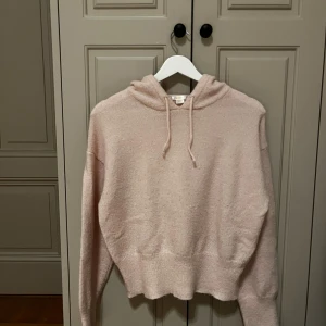 Ljusrosa hoodie från Gina Tricot - Supermysig ljusrosa hoodie från Gina Tricot i stickat material. Tröjan har huva med snörning, ribbad nederkant och långa ärmar. Perfekt för chill dagar och när du vill vara extra comfy. Croppad passform som ger en trendig look.