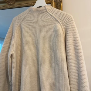 Beige ribbad stickad tröja med hög krage  - Säljer en beige stickad tröja i storlek S med ribbad struktur och hög hals. Tröjan har långärmade raglanärmar och är perfekt nu till vintern!!💕