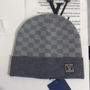 Grå rutig mössa från L och V - Snygg grå mössa från L och V med klassiskt rutigt mönster och uppvikt kant. L och V-logga framtill ger en exklusiv touch. Perfekt accessoar för kyliga dagar och stilrena outfits.