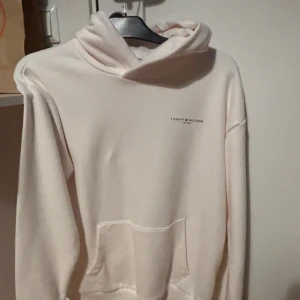 Ljus hoodie från Tommy Hilfiger - Säljer en stilren ljus hoodie från Tommy Hilfiger med diskret logga på bröstet. Tröjan har huva, magficka och långa ärmar. Perfekt för dig som gillar enkel och klassisk streetstyle. Endast andvänd 4 gånger. 