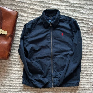 Ralph Lauren jacka - Säljer en stilren jacka från Ralph Lauren i marinblå med röd logotyp. Använd ett fåtal gånger och mycket bra skick. Passar för dig som är runt 160 cm. Kom med Bud! 
