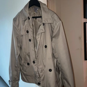 Kort trenchcoat - Kort trenchcoat ifrån HM Använd kanske 1-3 gånger har bara legat i förrådet och glömt att jag har den  Är en storlek 52 men skulle säga att den sitter som en M och jag själv är 181cm Så där av har jag tryckt i storlek M    Inte några skador eller något ytligt skulle säga att den är som ny bara lite ”dammig”  Vid frågor eller mer bilder så är det bara att skriva  OBS FINNS UTE PÅ FLER SIDOR