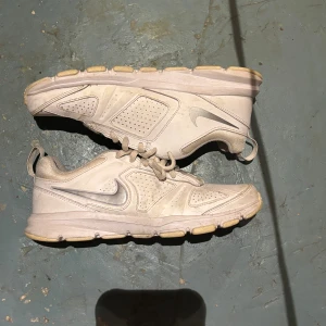 Nike T-Lite XI vita sneakers strl 37.5 - Nike T-Lite XI sneakers i ljusvit färg med grå detaljer och klassisk swoosh på sidan. Skorna har snörning, perforerade paneler för ventilation och en robust, mönstrad sula för bra grepp. Tillverkade i syntetmaterial och mesh för extra komfort.