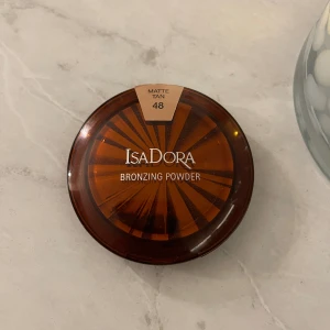 IsaDora Bronzing Powder Matte Tan 48 - Bronzing powder från IsaDora i nyansen Matte Tan 48. Kommer i en rund, brun plastförpackning med spegel i locket. Pudret har en matt finish och ger en naturligt solkysst look. Perfekt för att skulptera och ge värme till ansiktet.