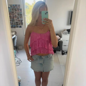 Rosa volangtop från Zara - Supersöt rosa topp från Zara med tunna axelband och flera lager volanger. Toppen är croppad och har en cool textur i tyget som ger extra liv. Perfekt för sommarens alla häng! Färgen är klar rosa och materialet känns lätt och luftigt.