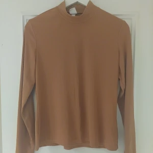 Beige polotopp med lång ärm - Säljer en stilren beige polotopp med lång ärm. Toppen har en enkel design med hög hals och är tillverkad i ett mjukt material som känns skönt mot huden. Perfekt att matcha med jeans eller kjol för en clean look.