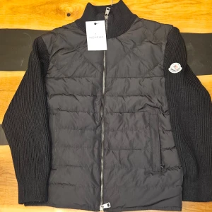 Moncler cardigan  - Moncler cardigan   Stilren och exklusiv Moncler cardigan med dunvadderad front och stickade ärmar. Perfekt för vår, höst och milda vinterdagar. Moncler-patch på vänsterärmen.  Äkta - originaltagg sitter kvar  Fint skick, sparsamt använd  Lätt, varm och superbekväm  Färg: Svart  Full zip + två dragkedjefickor  Storlek: M - sitter även bra på S för en lite mer relaxed passform.                  Anledningen till att jag säljer den är för att fick den av min morbror och säljer den åt honom.