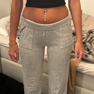 Grå Juicy couture mjukisbyxor  - Säljer ett par grå mjukisbyxor med bred resår i midjan och snörning framtill. Byxorna har två stora fickor fram och två bakfickor med lock och knappdetalj. Perfekta för chill dagar och riktigt sköna att ha på sig.