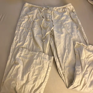 Beiga linnebyxor från Isolina Sartini - Snygga och luftiga linnebyxor från Isolina Sartini i beige ton. Byxorna har breda ben, stora fickor framtill och snörning i midjan för extra chill passform. Perfekta för varma dagar och enkel att matcha med en t-shirt eller skjorta.