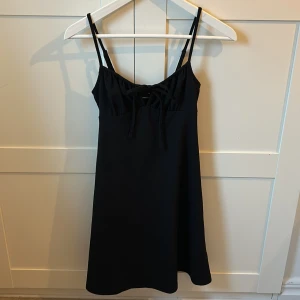 Svart kort klänning från Gina Tricot - Supersnygg svart klänning från Gina Tricot i storlek XXS. Modellen är kort med smala axelband och har en söt snörning framtill vid bysten. Materialet är lätt strukturerat och ger en cool känsla. Perfekt för dig som gillar enkel och stilren design.