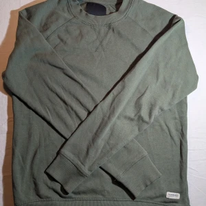 Grön sweatshirt - Säljer en stilren grön crewneck från lager 157 storlek S. Tröjan har klassisk rund halsringning, ribbade muddar och är tillverkad i mjuk bomull. Perfekt för lager-på-lager och chill vardagsstil.
