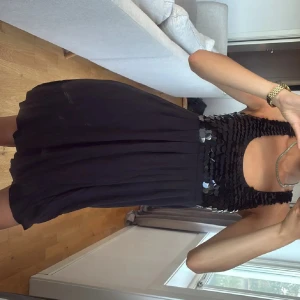 Svart paljettklänning med öppen rygg - Supersnygg svart kortklänning med paljetter upptill och öppen rygg. Klänningen har en luftig kjol och breda axelband. Perfekt för dig som vill sticka ut lite extra.