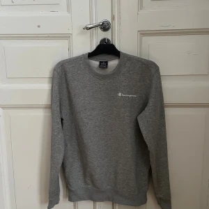 Grå sweatshirt från Champion - En stilren grå sweatshirt från Champion i storlek medium. Tröjan har rund halsringning, långa ärmar och diskret Champion-logga broderad på bröstet. Perfekt basic-plagg i mjuk bomullsblandning som funkar året runt.