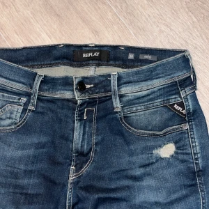 Replay Anbass jeans blå, storlek 30/34 - Snygga Replay Anbass jeans i mörkblå tvätt med slitningar och distressed detaljer. Klassisk femficksmodell med vita kontrastsömmar och Replay-logga på fickan. Smal passform och raka ben, tillverkade i stretchigt jeanstyg för skön känsla. Passar mig bra som är 189 cm. Hör av er vid funderingar!
