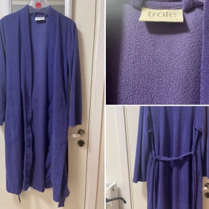 Lila morgonrock - Säljer en lila cardigan jacka från Trofé med långa ärmar och knytband i midjan. Jackan har två fickor framtill och är tillverkad i mjukt stickat material. Perfekt för att slänga över en outfit när du vill ha något bekvämt och snyggt.