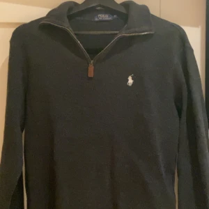 Svart half zip tröja Polo Ralph Lauren - Svart långärmad tröja från Polo Ralph Lauren med half zip och klassisk vit logga på bröstet. Tröjan har en stilren krage och är perfekt för dig som gillar en clean och tidlös look. Passar till allt och är riktigt skön att bära.
