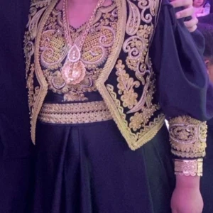 Traditionell albansk demije i svart och guld dallama  - Unik svart långklänning med puffärmar och detaljerad guld brodyr. Klänningen har matchande väst med blommiga och snirkliga mönster i guld, samt bredt bälte i midjan. Tillverkad i glansigt tyg som ger en lyxig känsla. Perfekt för dig som vill sticka ut.