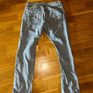 G-Star Raw ljusgrå jeans - Storlek 30/30.  Snygga ljusgrå jeans från G-Star Raw med klassisk femficksdesign och raka ben. Jeansen har en normal passform och är tillverkade i mjukt denimtyg. Perfekta för dig som gillar stilrena och moderna jeans med diskret branding på bakfickan.