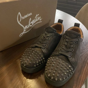 Christian Louboutin gråa sneakers med nitar - Unika svarta sneakers från Christian Louboutin i mocka med coola grå nitar på tån och klassisk röd sula. Det saknas 2-3 spikar inget som stör, en lyxig känsla med läderdetaljer invändigt. Lådan ingår ej tyvärr 