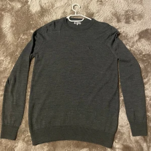 Mörkgrå stickad tröja Lee Cooper - Snygg mörkgrå stickad tröja från Lee Cooper med diskret logga på bröstet. Rund halsringning och ribbade muddar vid ärmslut och nederkant. Använd ett fåtal gånger så väldigt fin. 