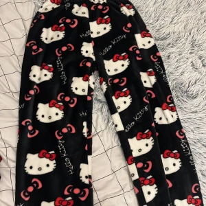 Hello Kitty fleecebyxor svart/rosa - Mysiga fleecebyxor med Hello Kitty-motiv i vitt och rosa på svart botten. Byxorna har elastisk midja och är täckta av söta rosetter och Hello Kitty-ansikten. Perfekta för chill eller sleepover.