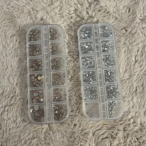 Strasstenar för naglar i två färger - Två askar med strasstenar i olika storlekar, en med silvriga och en med champagnefärgade stenar. Perfekta för att skapa kreativa naglar!Kommer i praktiska plastaskar med fack för enkel sortering.