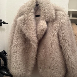 Beige pälsjacka från Zara - Säljer en fluffig och lyxig beige pälsjacka från Zara i storlek M. Jackan har bred krage och är helfodrad för extra komfort. Perfekt för dig som vill ha en statement piece med oversized känsla och mjuk päls-look.