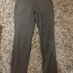 Grå kostymbyxor från Only & Sons - Snygga grå kostymbyxor från Only & Sons i stretchigt material. Byxorna har raka ben, diskreta sidofickor och knappar bak. Perfekta för en clean och stilren look. Materialet är en blandning av polyester, viskos och elastan för extra komfort.