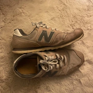 Beige New Balance sneakers med grå detaljer -  New Balance sneakers storlek 42,6, lite smutsiga men skulle tro att det går bort med en tvätt men inte testat själv, använt skick 