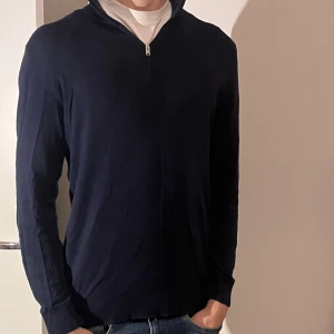 Mörkblå långärmad half zip tröja - Snygg mörkblå långärmad tröja med half zip framtill. Tröjan har en klassisk och stilren look med ribbade muddar vid ärmslut och nederkant. Perfekt för dig som gillar enkel och clean stil. Passar dig som vill ha en normal passform.