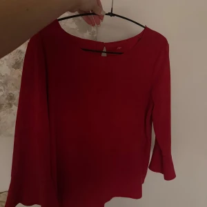 Röd blus från s.Oliver med trumpetärm - Röd blus från s.Oliver i storlek 36. Modellen har rund halsringning, långa ärmar med lätt trumpetformad avslutning och en liten knappdetalj bak i nacken. Enkel och stilren design som ger en snygg look.