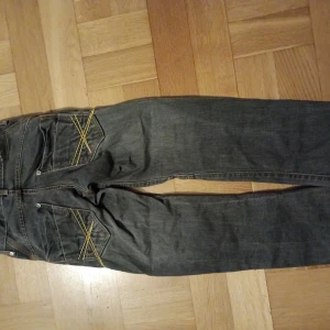 Mörkgråa jeansbyxor med kontrastsömmar stl 134 pojke  - Säljer ett par mörkgråa jeansbyxor från Diesel med raka ben och snygga kontrastsömmar i gult och orange. Bakfickorna har coola dekorativa sömmar som sticker ut. Klassisk femficksmodell och bälteshällor. Perfekta för dig som gillar streetstil. Inköpta hos Lindex och sparsamt använda. Stl 134 för pojke.