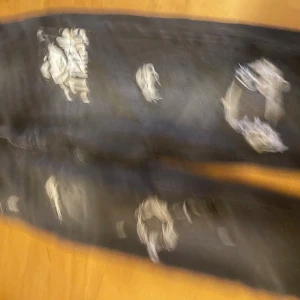 Svarta ripped jeans från FSBN - Svarta jeans från FSBN med coola slitningar och trasiga detaljer på benen. Jeansen har en rak passform och patch med tryck på ena låret. Perfekt för dig som gillar en edgy streetstil. Materialet är klassisk denim och midjan är normal.