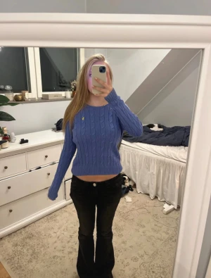 Blå stickad tröja Polo Ralph Lauren - Säljer en blå, croppad stickad tröja från Polo Ralph Lauren i mjuk pima bomull. Tröjan har kabelstickat mönster, lång ärm och gul broderad logga på bröstet. Perfekt för dig som gillar klassisk stil med en modern twist.