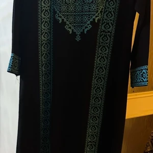 Svart klänning med broderi - Elegant svart klänning med intrikata blå broderier längs framsidan och ärmsluten. Klänningen har en lång design , vilket ger en sofistikerad look. Perfekt för speciella tillfällen.