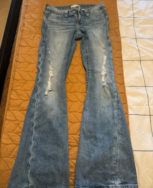 Gina 14+ Jeans  - Bootcut jeans i ljusblå denim med slitna detaljer på framsidan av benen och rå kant längst ner. Klassisk femficksmodell med låg midja och snygga sömmar på bakfickorna. Perfekt för dig som gillar retrovibbar och avslappnad stil.