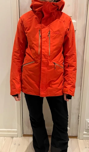 Röd/orange skidjacka från Everest - Super fin röd/orange skidjacka från Everest. Den har snölås och är typ helt ny, super super fint skick. Har liftkortsficka i armen, fickor vid bröstet samt där nere vid midjan. Har även ventileringsficka. Hög och gosig krage. 