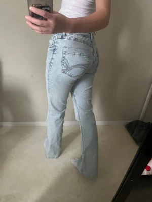 Ljusblå bootcut jeans från Hm - Snygga ljusblå jeans från hm med klassisk femficksdesign och bootcut-ben. Jeansen har låg midja och raka ben med lätt utsvängning nedtill. Tillverkade i mjukt denim med subtila slitningar och hm broderi på bakfickan.