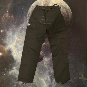 Svarta cargopants från Corteiz  - Svarta cargopants från Corteiz med flera stora fickor på benen och patchdetaljer med texten 'Guerillaz' och 'Rules the World'. Helt oanvända fraktas 24 timmar efter köpet. Från Goat