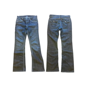 Dry Aged Denim bootcut jeans blå - Snygga blå jeans från Dry Aged Denim i bootcut-modell med klassisk femficksdesign och kontrastsömmar. Jeansen har låg midja, dragkedja och knapp framtill samt detaljerade bakfickor. Perfekt för dig som gillar en tidlös och cool look.